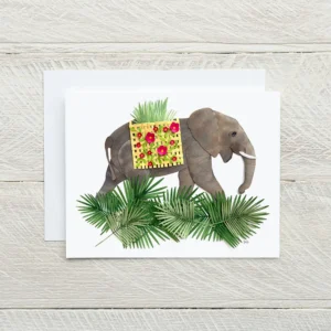 Paper sculpture greeting card showing a gray elephant carrying a basket of red flowers surrounded by tropical palm fronds